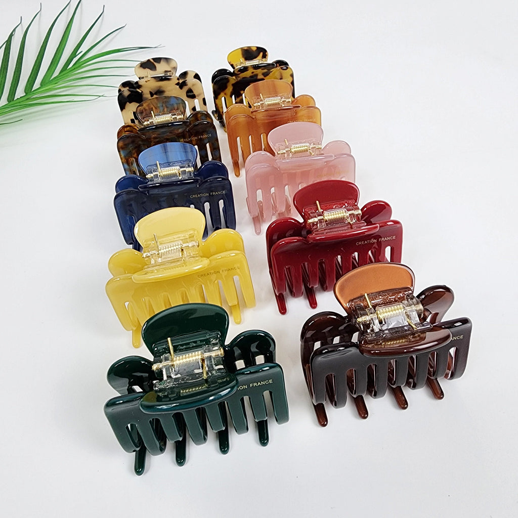 Cellulose acetate zigzag hair claw clip in tortoise shell and solid colors. Small 2.2 inch glossy nonslip jaw clamp for women creating half updo hairstyles. A set of ten hair claw clips in various colors including brown, yellow, green, red, orange, blue, and pink. The clips are made of plastic and have a textured finish. Each clip has a gold metal spring and the words 'Creation France' printed on the side.