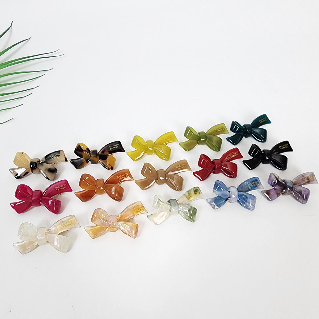 Cellulose acetate hair barrette featuring a small double bow design. 1.8 inch alligator clip available in 15 colors including tortoise shell and aurora finishes. Perfect for side bangs or toddler hairstyles.