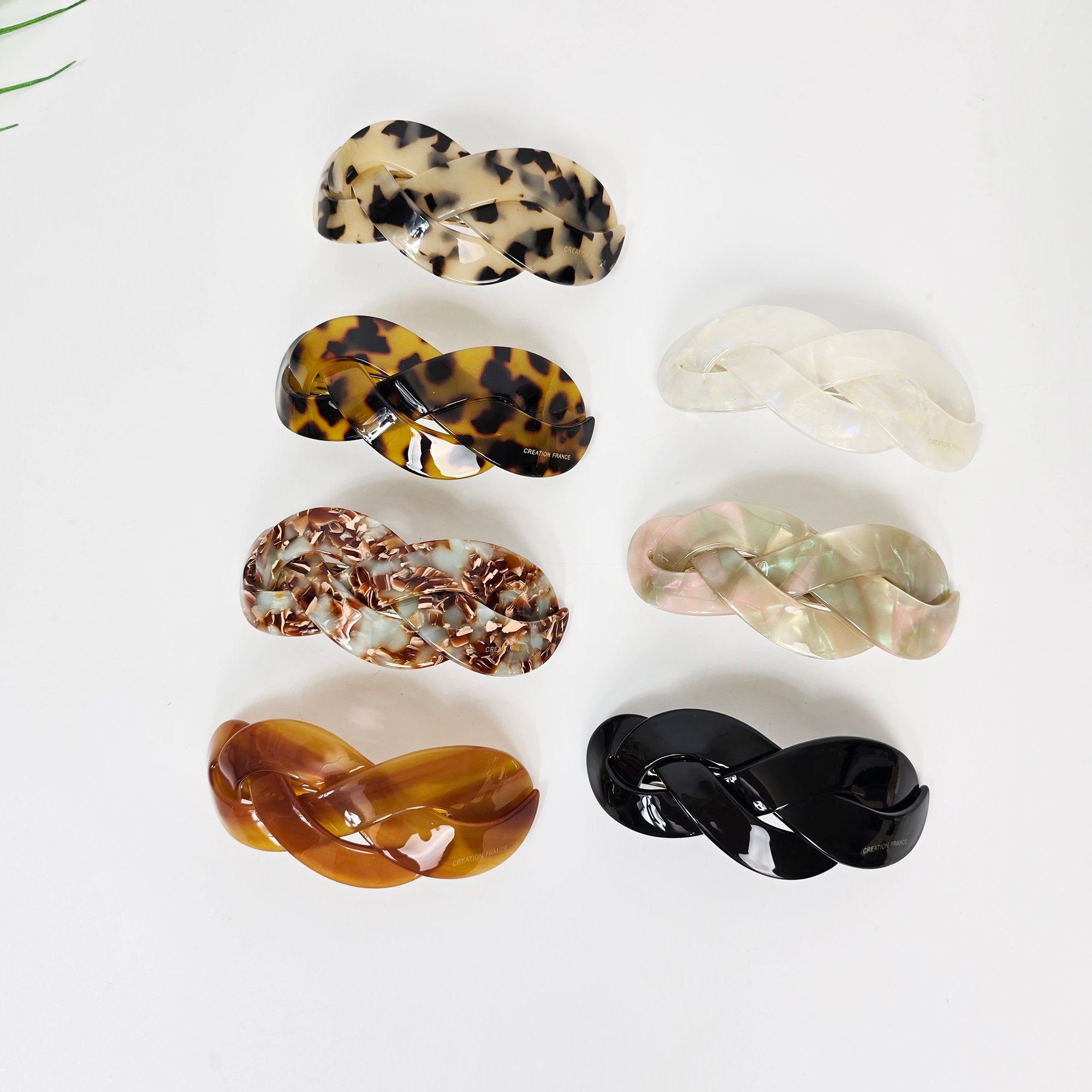 Cellulose acetate triple twist hair clip, curved french barrette in tortoise shell and pearl colors, elegant half up ponytail holder. Six braided hair clips in various colors and patterns. The clips are made of plastic and have a glossy finish. The colors include brown, black, white, and beige. The patterns include leopard print, tortoise shell, and a marbled pattern.