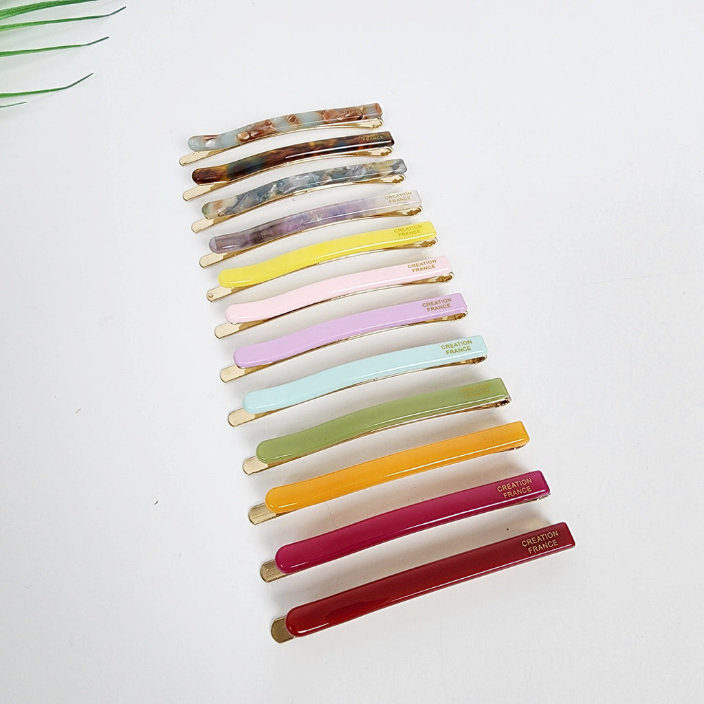Cellulose acetate bobby pins in pastel and tortoise shell patterns. Slim 2.4 inch straight hair slides with gold tone hardware. Minimalist side bang clips for women and girls. A collection of colorful hair barrettes. The barrettes are in various colors including marbled, brown, purple, yellow, pink, lavender, teal, olive green, orange, burgundy, and deep red. Each barrette has a gold-colored metal base and the words 'CREATION FRANCE' printed on it.