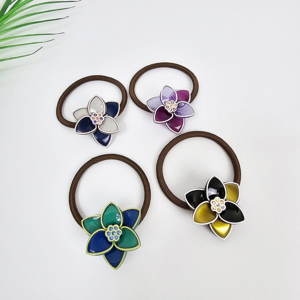 Cellulose acetate lotus flower hair tie with crystal center and gold outline. Elegant floral ponytail holder in navy purple green and black. Korean hair accessory. Four hair scrunchies with different colored flower charms. One scrunchie has a white and blue flower charm, one has a purple flower charm, one has a green and blue flower charm, and one has a black and gold flower charm.