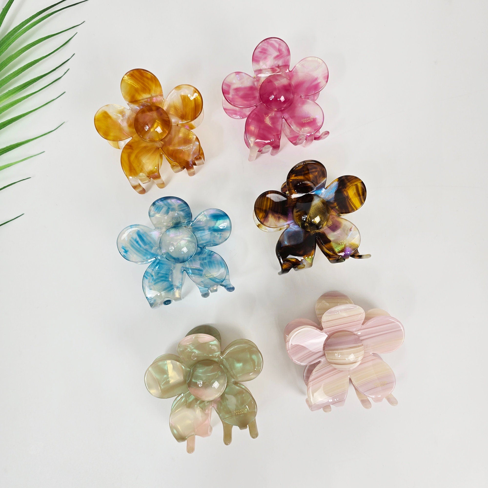 Cellulose acetate flower hair claw clip in pastel aurora colors, large floral jaw clamp for thick hair updo, cute summer accessory. Six flower-shaped hair clips in various colors and patterns. The clips are made of plastic and have a shiny finish. The colors include pink, brown, blue, green, and yellow.