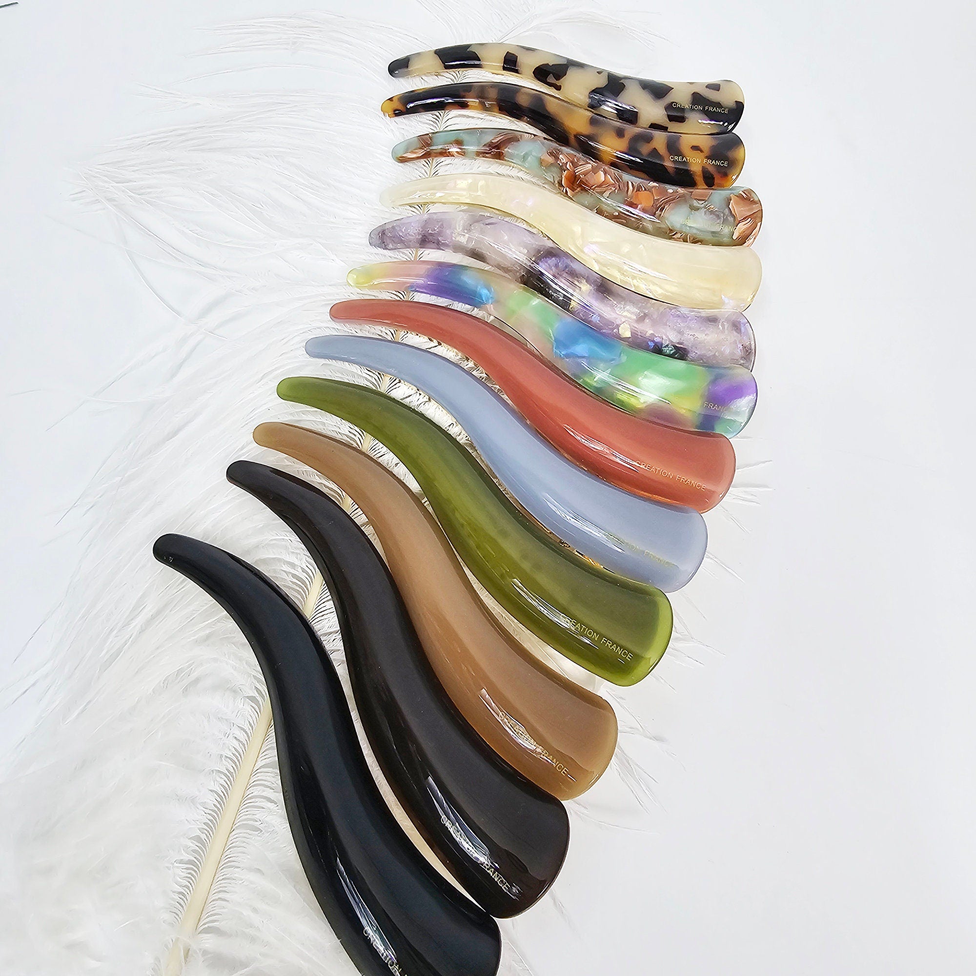 Long curved alligator hair clip in cellulose acetate. Tortoise shell and solid color beak barrette for french twist updos. A set of 14 assorted hair clips in various colors and patterns. The clips are made of plastic and have a curved, horn-like shape. The clips are arranged in a stack, with the largest clip at the bottom and the smallest clip at the top. The clips are all made in France.