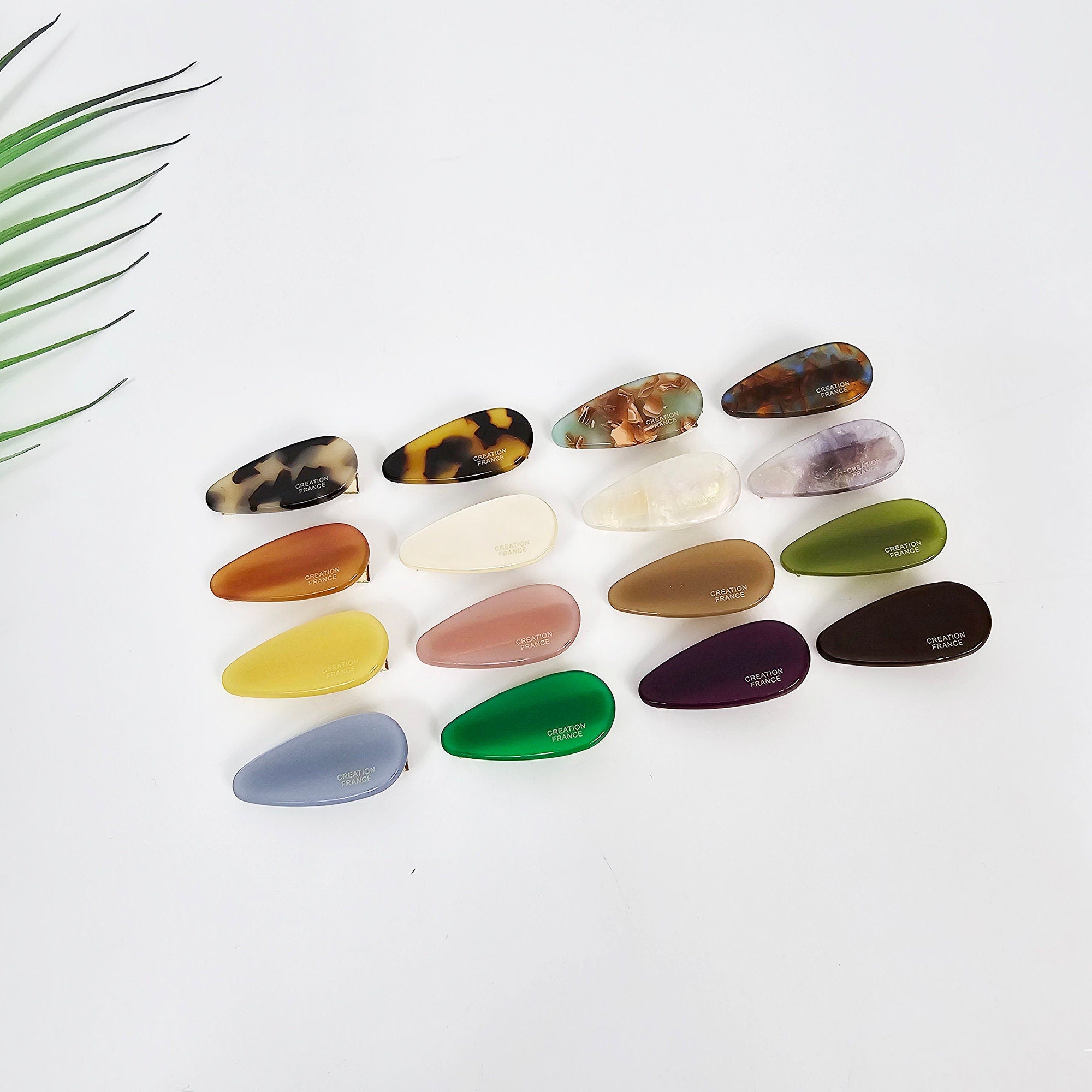 Mini rounded triangle alligator hair clips in tortoise shell and vivid colors. Small 1.4 inch cellulose acetate beak clips for side bangs. Cute hair accessories for women and toddlers. A collection of 15 teardrop shaped hair clips in various colors including green, purple, blue, yellow, brown, and white. The clips have the words 'CREATION FRANCE' printed on them.
