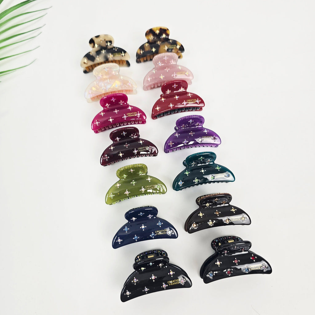 Small cellulose acetate hair claw clip with rhinestone crystals. 1.9 inch half moon design with double interlocking teeth for secure half-up styling. A collection of twelve hair clips in various colors including pink, purple, green, blue, and black. The clips are decorated with rhinestones and have the words 'CREATION FRANCE' printed on them.