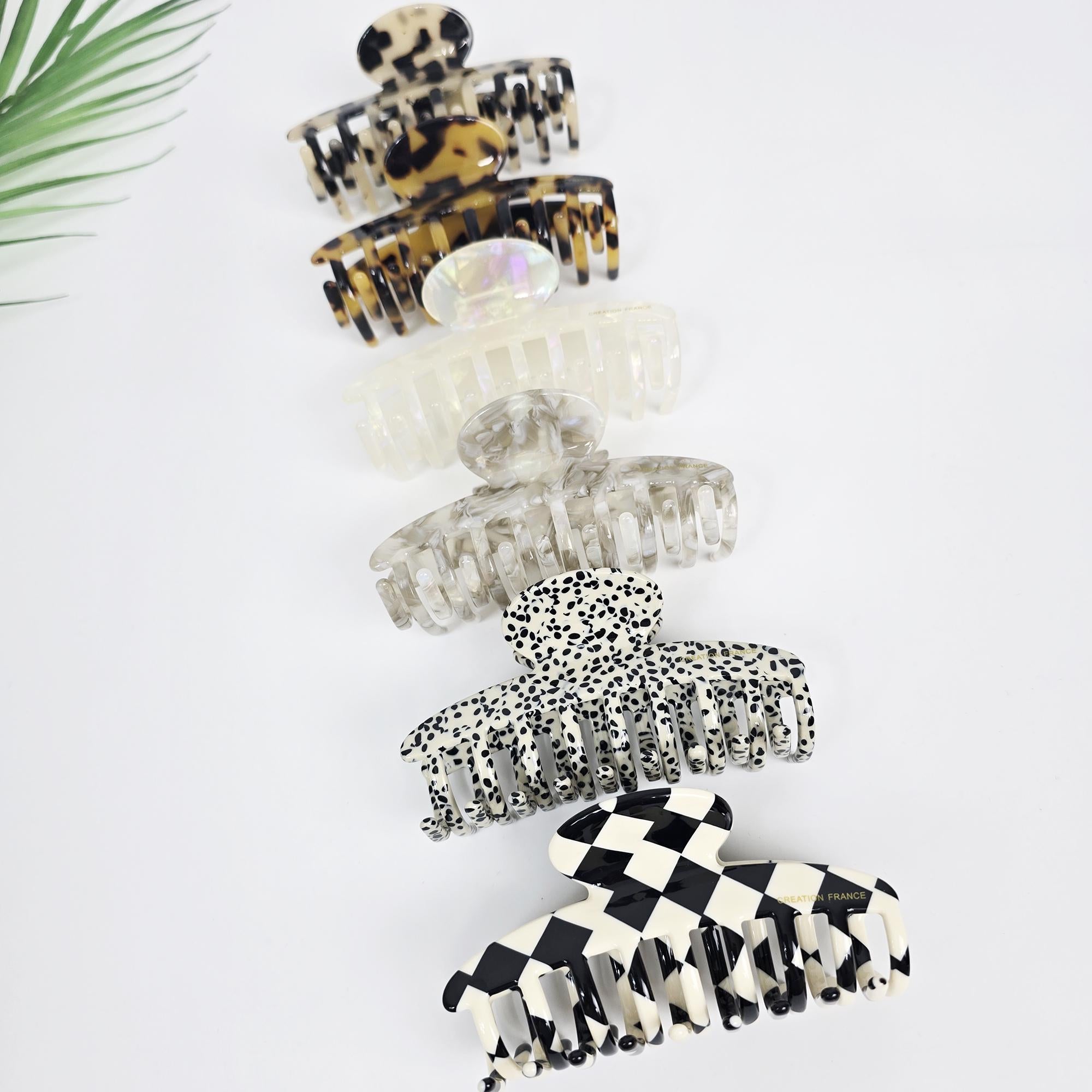 Cellulose acetate hair claw clip in tortoise shell and checkerboard patterns. Curved 3.8 inch jaw clip for thick hair updos and minimalist styling. A set of six hair claw clips. The clips are made of clear plastic with different patterns. The patterns include leopard print, iridescent, white polka dots, black polka dots, and black and white checkered.