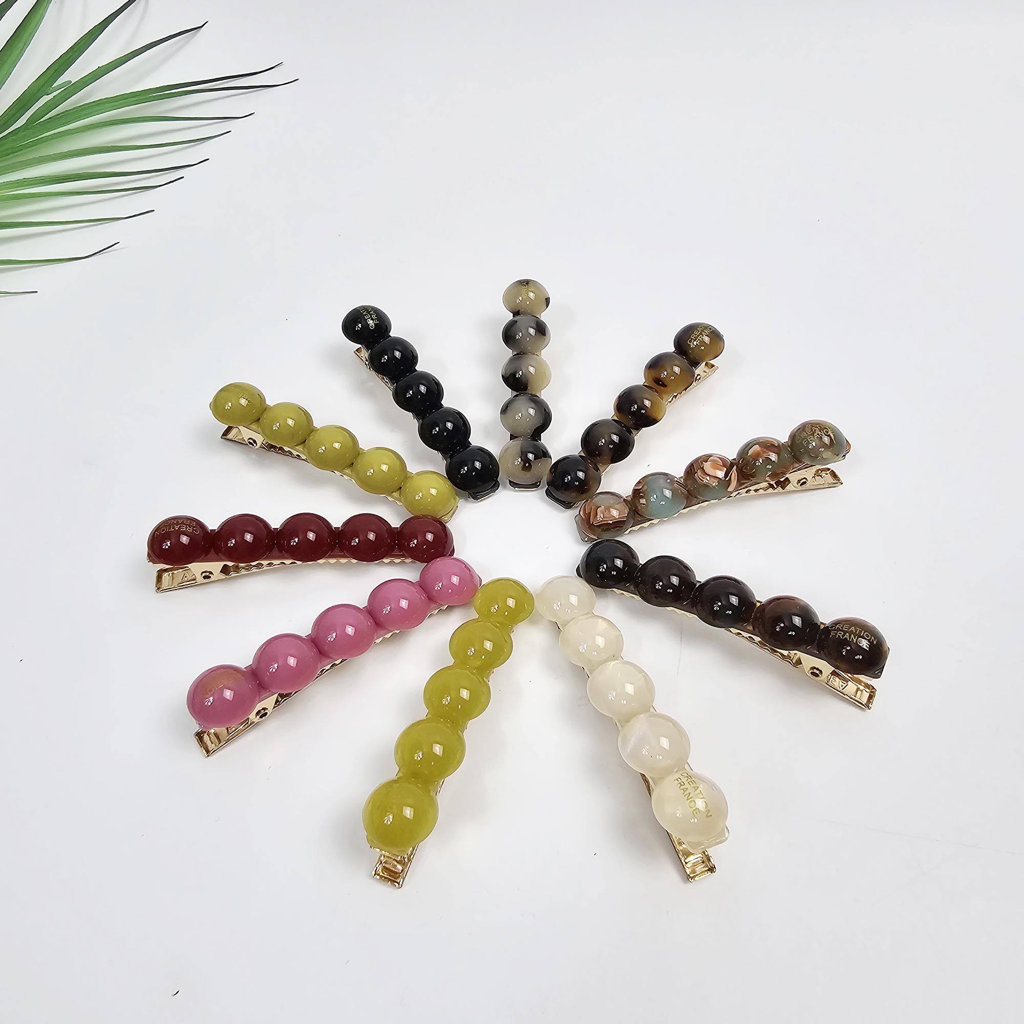 Cellulose acetate bubble hair clip in tortoise shell and solid colors. Geometric water drop barrette for holding side bangs comfortably. Assortment of hair clips featuring rows of colorful resin beads.  Clips include shades of green, pink, brown, beige, and dark brown. Each clip has a gold-toned metal bar.  These beaded hair accessories are ideal for adding a touch of elegance to any hairstyle.