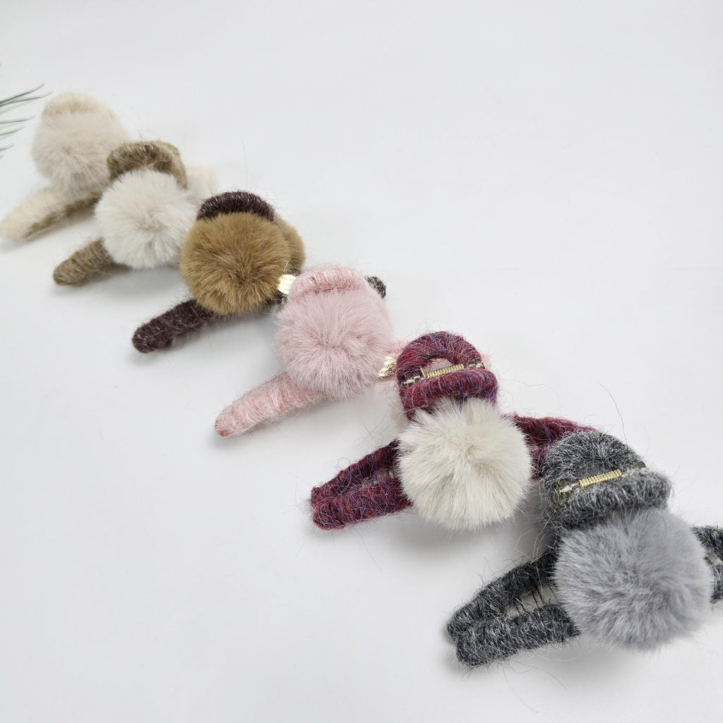 Large knitted hair claw clip wrapped in soft yarn with a faux fur pom-pom accent. 5.1 inch oversized jaw clip designed for holding thick hair updos. Cozy winter hair accessory available in beige and neutral tones.