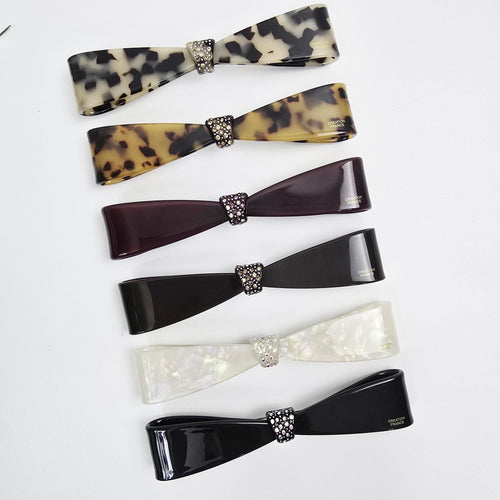 Cellulose acetate long slim hair barrette with a rhinestone bow tie accent. 4.9 inch automatic french clip suitable for ponytails or half-up styles. Elegant hair accessory.