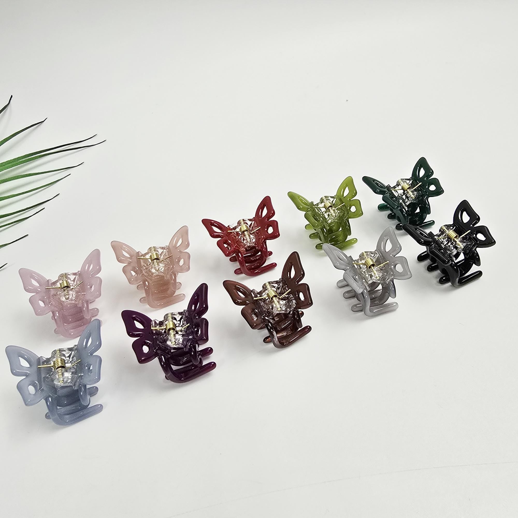 Cellulose acetate mini butterfly hair claw clip with crystal accent. 1.2 inch small jaw clip available in 10 colors. Perfect for toddler girls or styling bangs. Ten butterfly shaped hair clips in various colors including pink, red, purple, green, and gray. The clips are made of plastic and have a shiny finish.