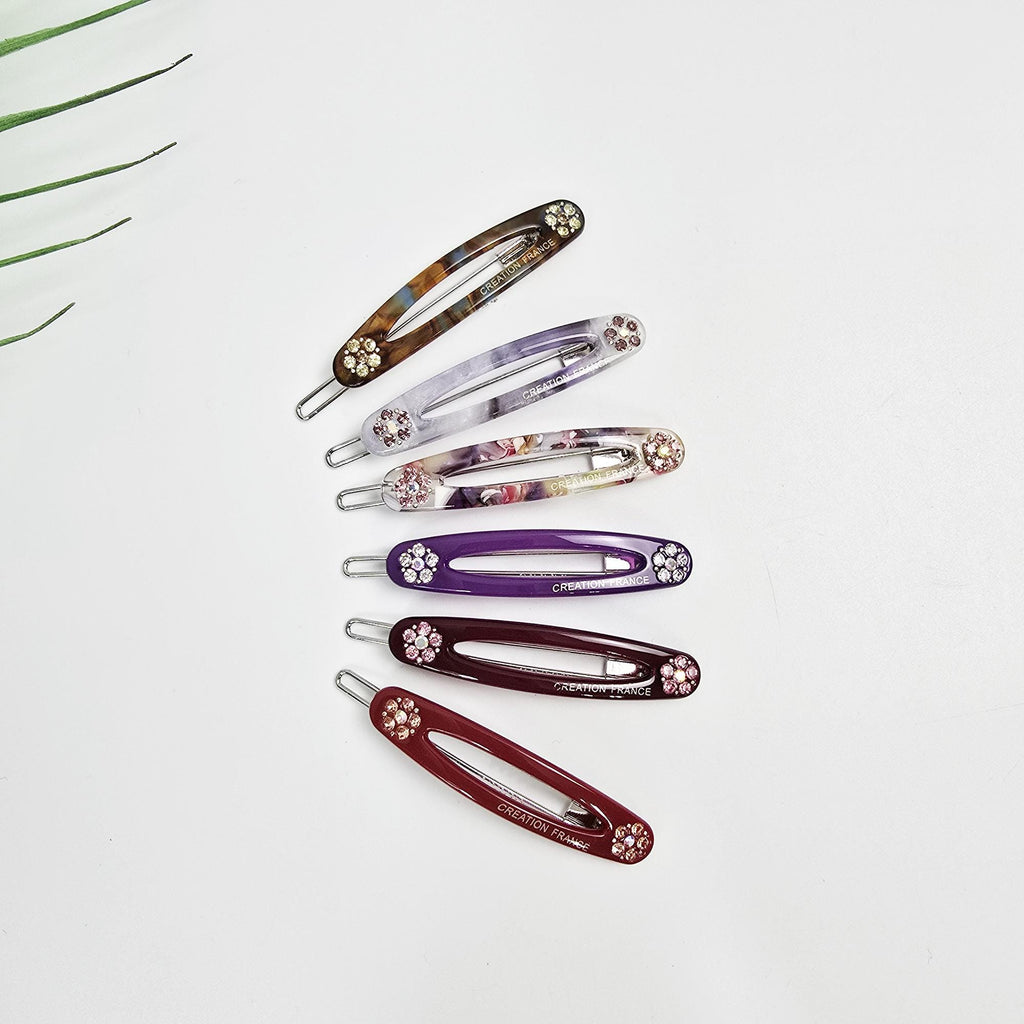 Cellulose acetate oval snap hair clip featuring delicate rhinestone floral accents. 2.2 inch french barrette available in red, purple, and tortoise shell patterns. Perfect for securing side bangs with a touch of sparkle.