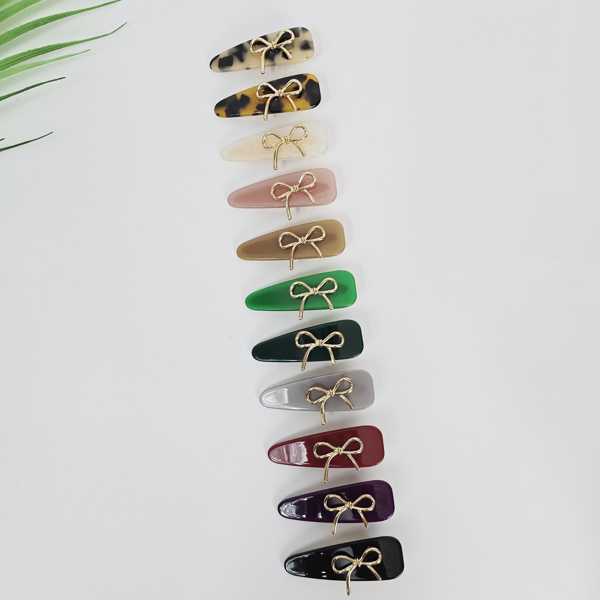 Cellulose acetate triangle hair clip with gold metal bow. Small 2.2 inch tortoise shell side barrette with alligator clip for girls and women. Twelve hair clips with gold bows. The clips are in various colors including brown, white, pink, beige, green, gray, red, purple, and black.