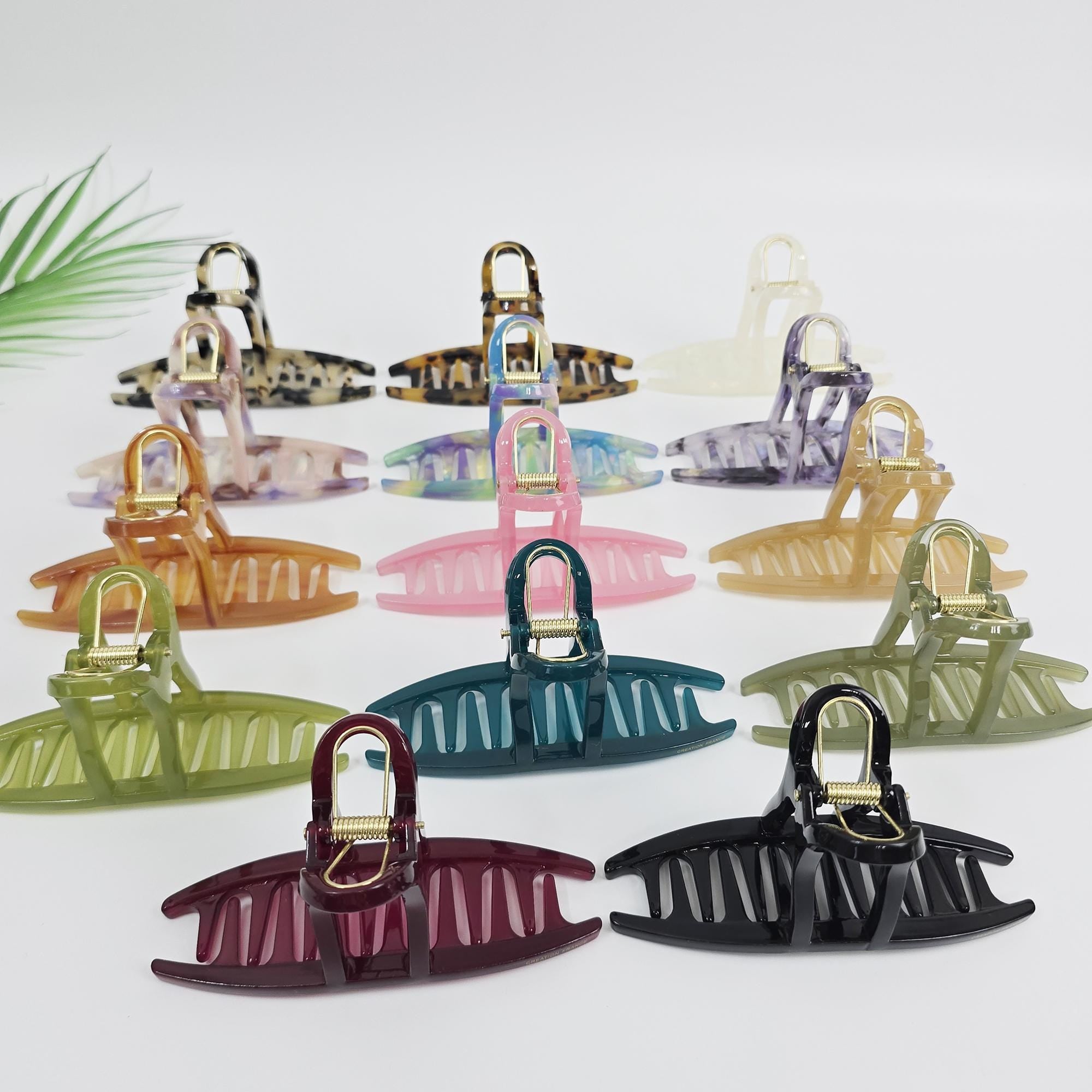 Large cellulose acetate hair claw clip featuring an open curved rectangular design. 4.7 inch tortoise shell and solid color jaw clamp for updos and French twists. A collection of 14 hair claw clips in various colors and patterns, including brown, green, black, pink, and purple. The clips are made of plastic and have a smooth, glossy finish. Each clip has a spring-loaded mechanism that allows it to securely hold hair in place.