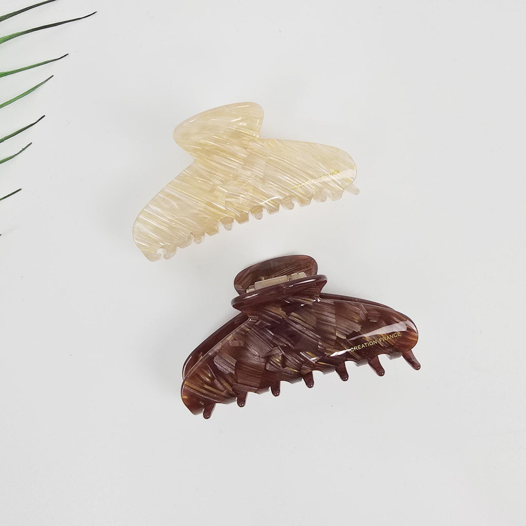 Cellulose acetate flat half-moon hair claw clip in marble beige and tortoise shell for elegant half-up hairstyles. Two hair clips, one is brown with a swirl pattern and the other is cream with a swirl pattern. The brown clip has the words 'CREATION FRANCE' printed on it.