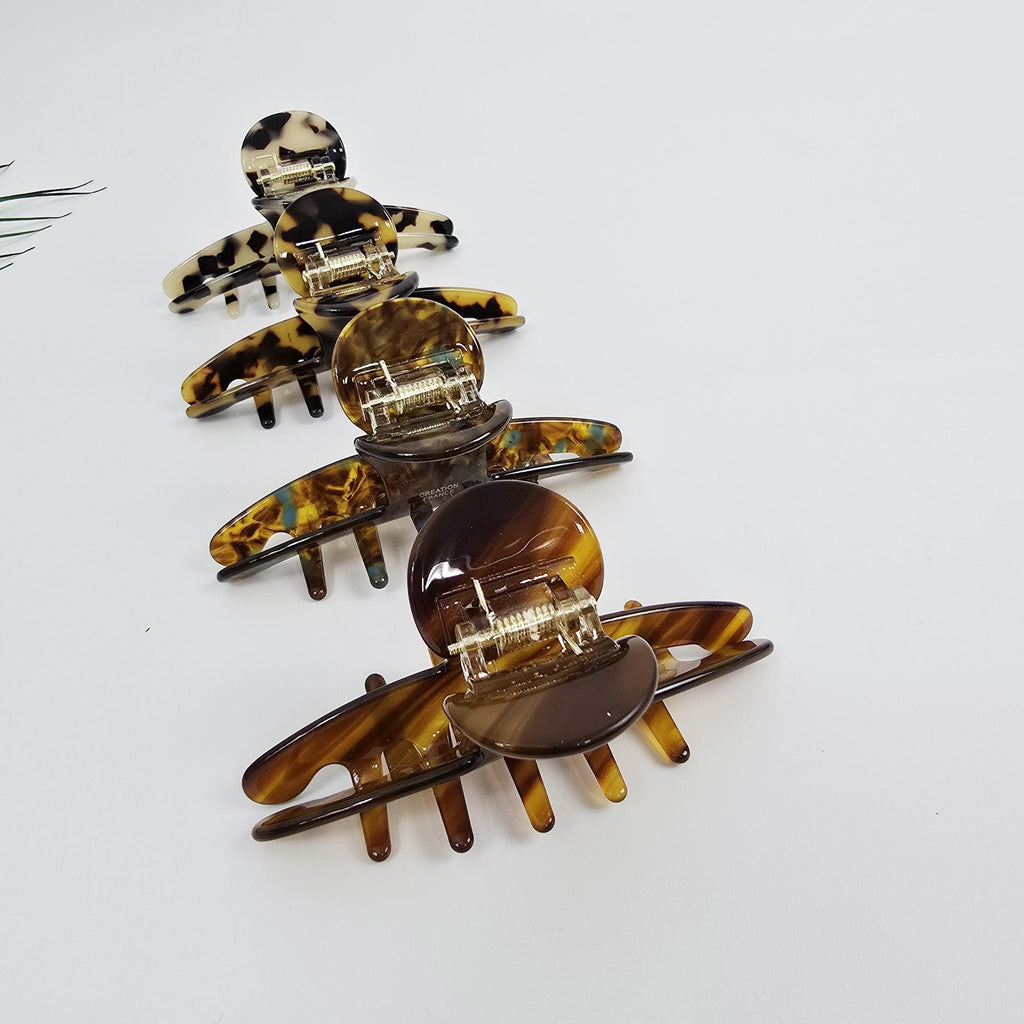 Cellulose acetate hair claw clip in tortoise shell. Glossy medium jaw clamp for women styling thick hair or elegant half-updos. Four brown and black tortoise shell hair clips with gold metal clasps. The clips are arranged in a row, with the largest clip at the bottom and the smallest clip at the top.