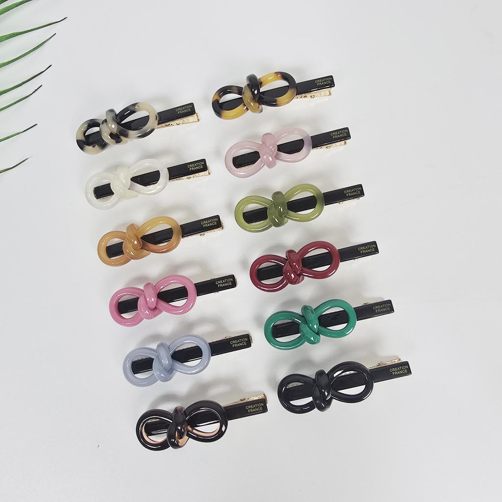 Cellulose acetate knotted bow hair clip with alligator slide mechanism in tortoise shell and pastel colors for side bangs styling.