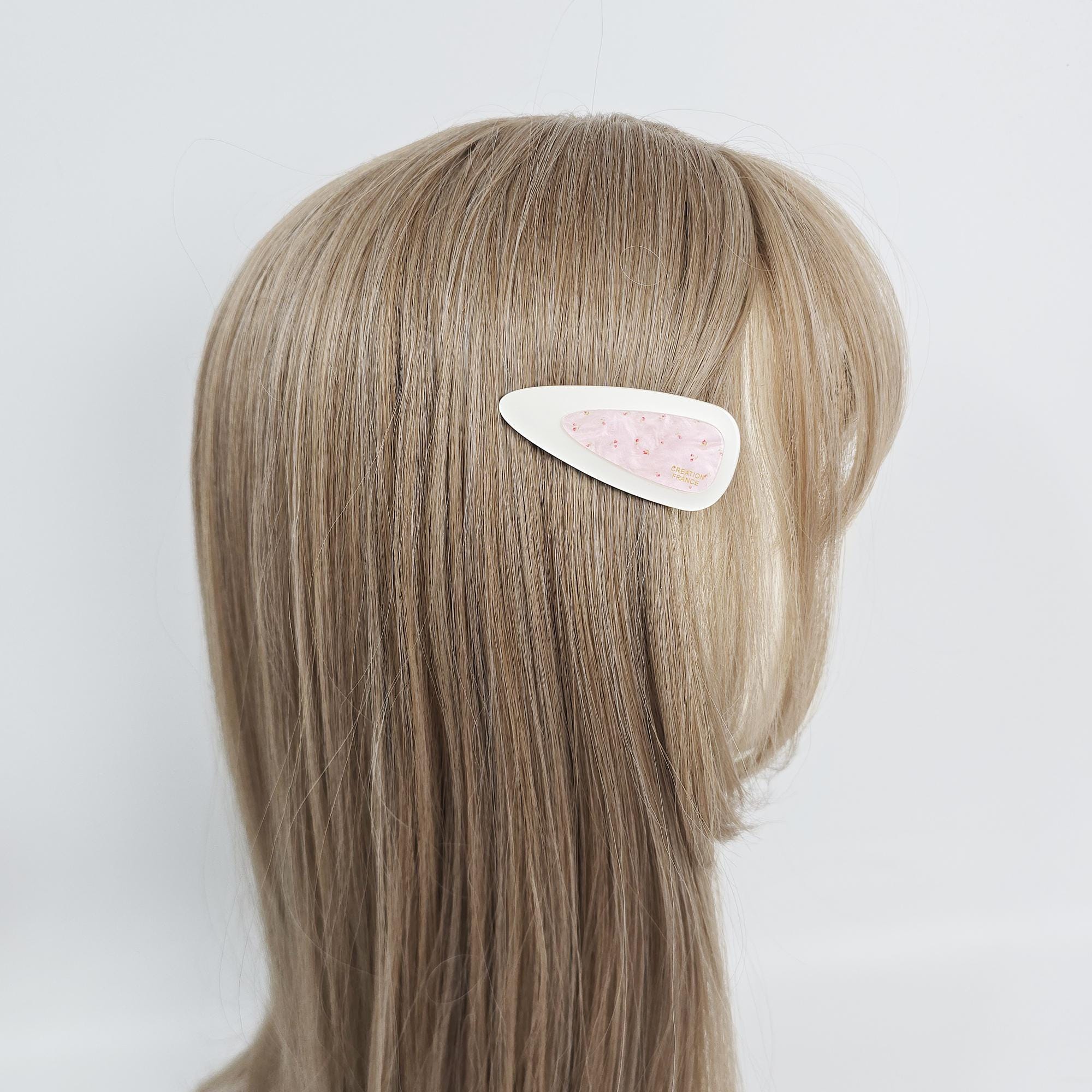 Cellulose acetate triangle snap hair clips featuring tortoise shell and pastel floral patterns for women and girls. A white hair clip with a pink floral design. The clip is in the hair of a person with light brown hair. The hair clip is a simple, decorative accessory. The floral design is a pattern of small pink shapes on a white background.