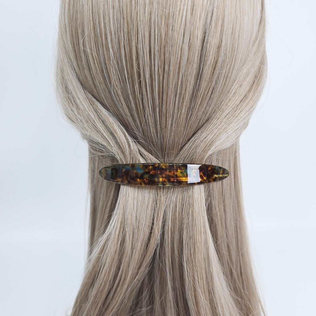 Cellulose acetate long slim curved barrettes in tortoise shell and pastel colors for half up hairstyles. A tortoiseshell hair clip with a rectangular shape. The clip is brown with yellow and black marbling. A white section is in the middle of the clip. The hair accessory is holding back blonde hair.