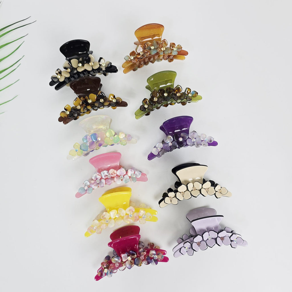Cellulose acetate floral hair claw clip with rhinestone accents and tortoise shell pattern for women styling thick hair. A collection of hair claw clips in various colors. The clips are adorned with flower-shaped embellishments. Colors include black, brown, orange, green, purple, pink, yellow, and lavender. The clips are arranged on a white surface.