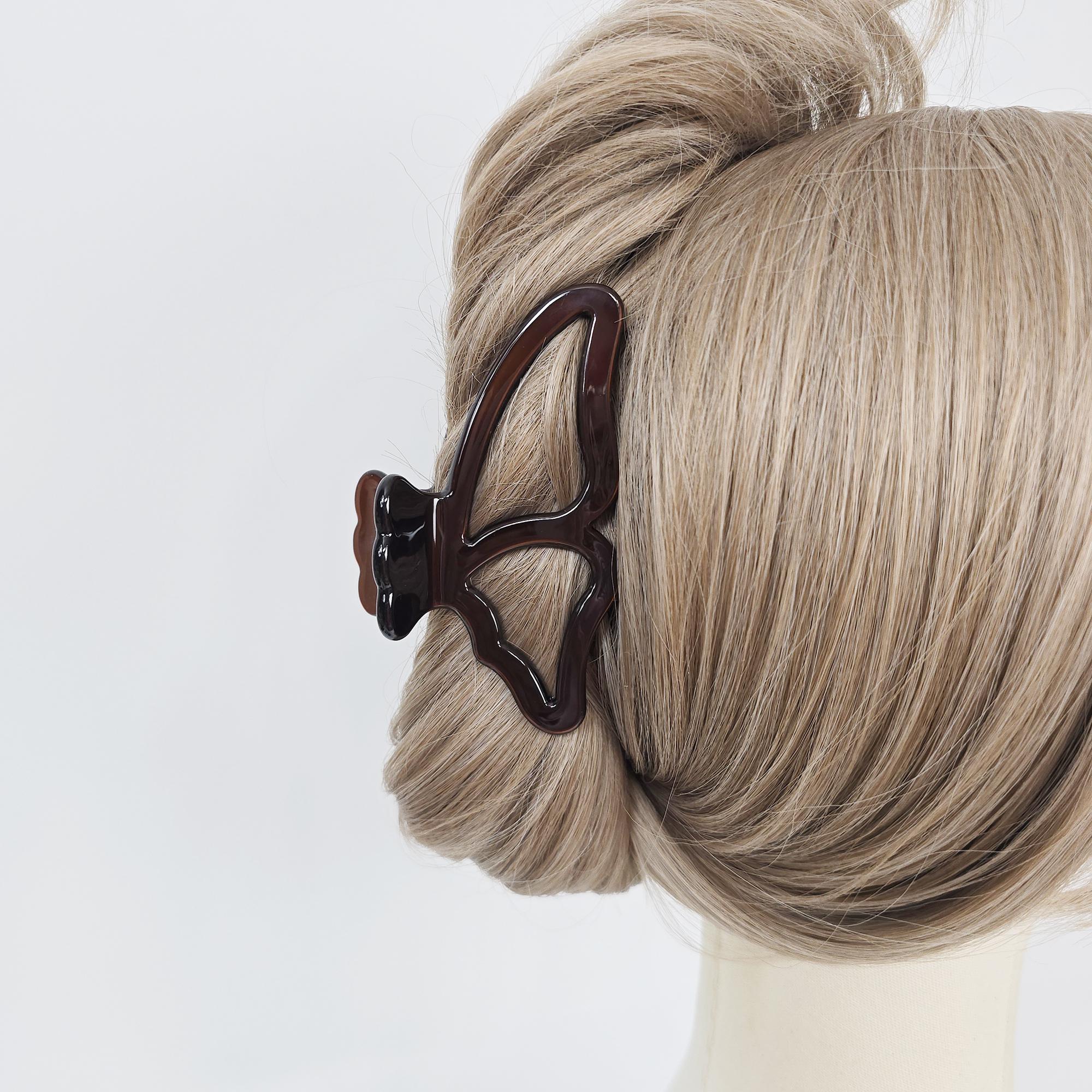 Cellulose acetate butterfly wing hair claw clip in tortoise shell and pastel colors for elegant updos. A dark brown butterfly hair claw clip is holding up a bun of light brown hair. The claw clip is made of plastic and has a butterfly shape with a matte finish. The hair is styled in a bun.